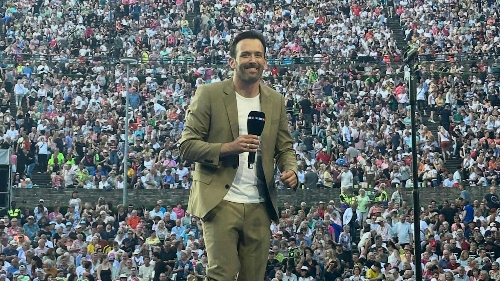 Ein Mann steht mit einem Mikro in der Hand auf einer Bühne.