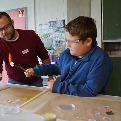 Das Bild zeigt einen Lehrer und einen Jungen bei einem chemischen Experiment mit Feuer.