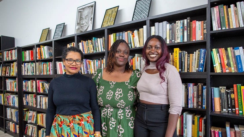 Glenda Obermuller (v.l.n.r.), N'joula Baryoh und Sängerin Naiyango stehen vor gefüllten Bücherregalen.