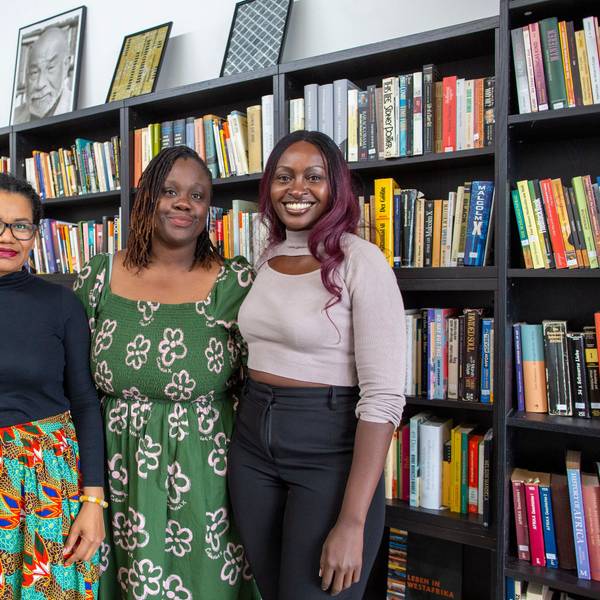 Glenda Obermuller (v.l.n.r.), N'joula Baryoh und Sängerin Naiyango stehen vor gefüllten Bücherregalen.