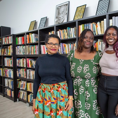 Glenda Obermuller (v.l.n.r.), N'joula Baryoh und Sängerin Naiyango stehen vor gefüllten Bücherregalen.
