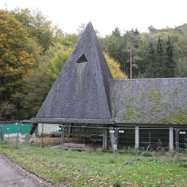 Ein Bauzaun umgibt eine Kapelle, auf deren Dach zum Teil grünes Moos wächst.