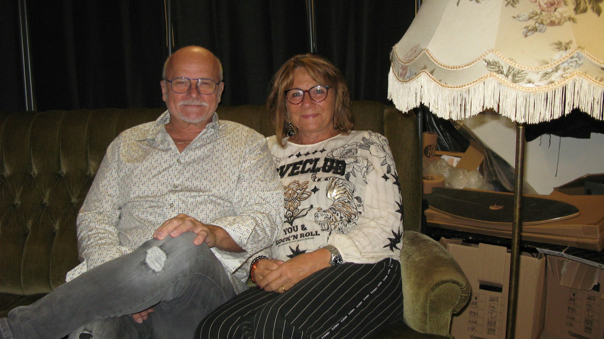 Ingo und Gaby Teusch sitzen auf dem Hennefer Sofa, rechts daneben steht eine altmodische Stehlampe.