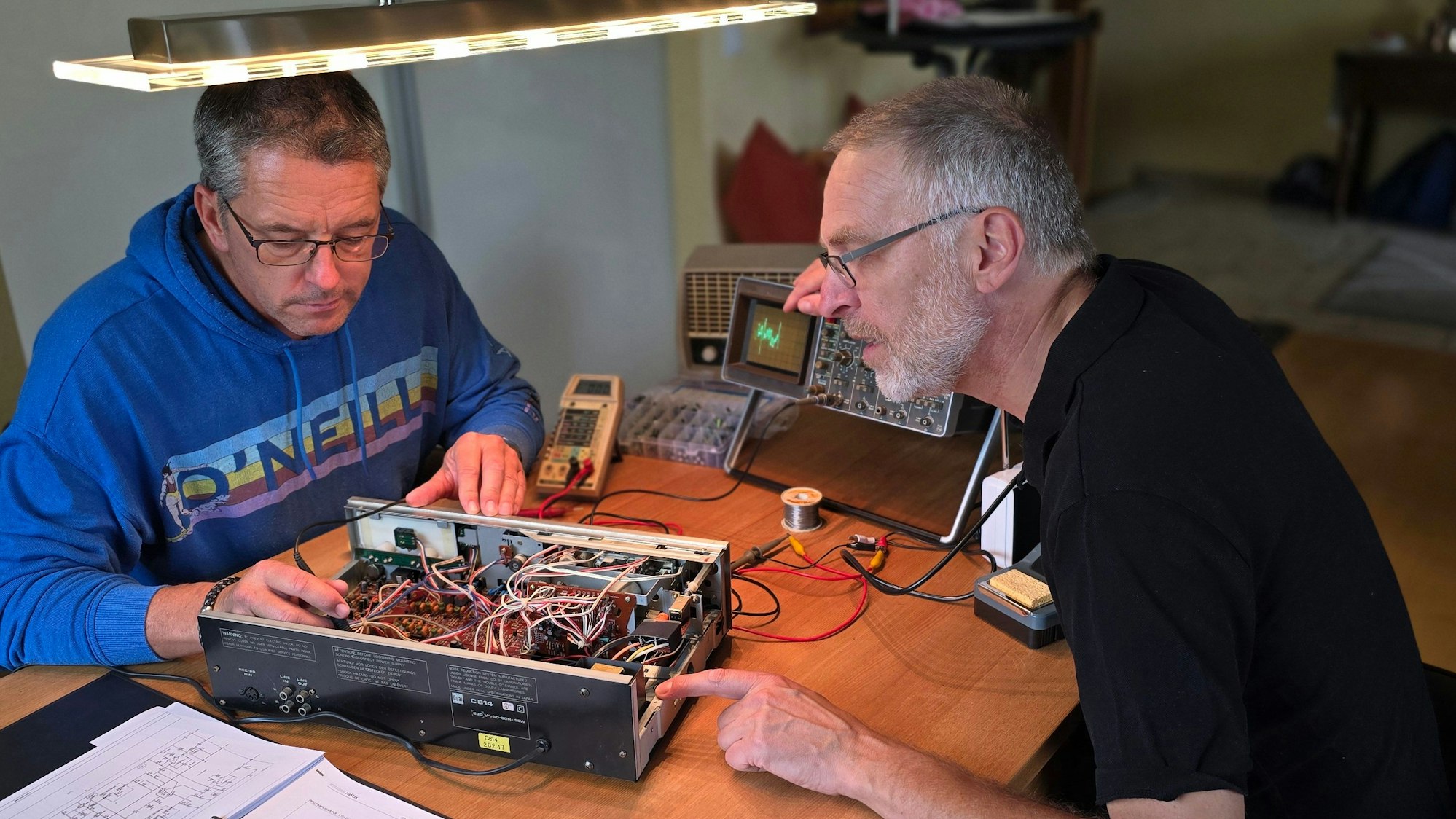 Zwei Männer haben das Gehäuse eines elektrischen Gerätes geöffnet und suchen nach einem Defekt.