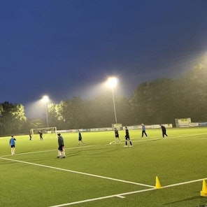 Auf dem Bild ist der beleuchtete Platz zu sehen, einige Kinder spielen Fußball.