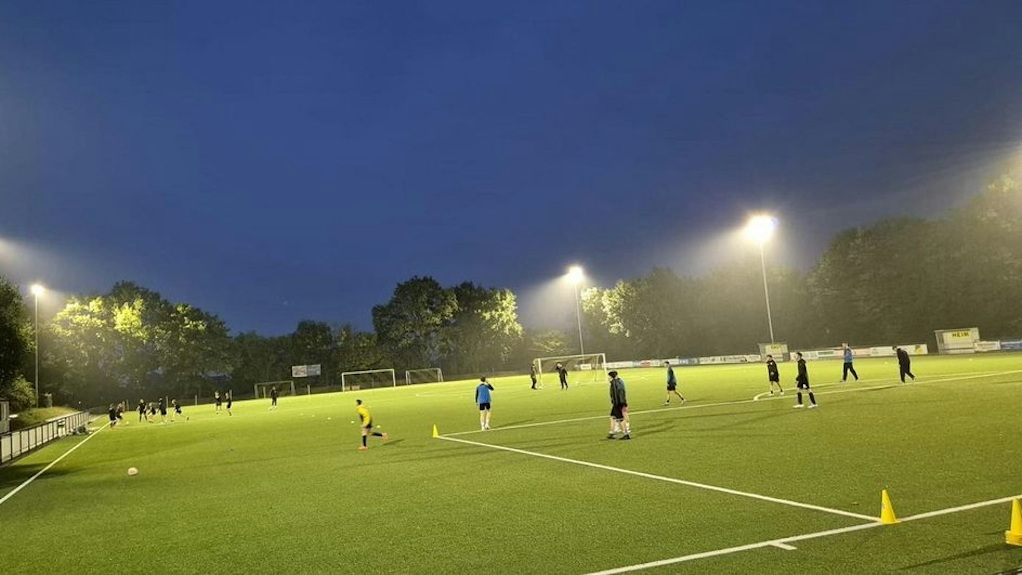 Auf dem Bild ist der beleuchtete Platz zu sehen, einige Kinder spielen Fußball.