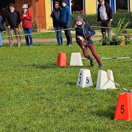 Das Bild zeigt das Mädchen, wie es mit einem Steckenpferd einen Parcours bewältigt.