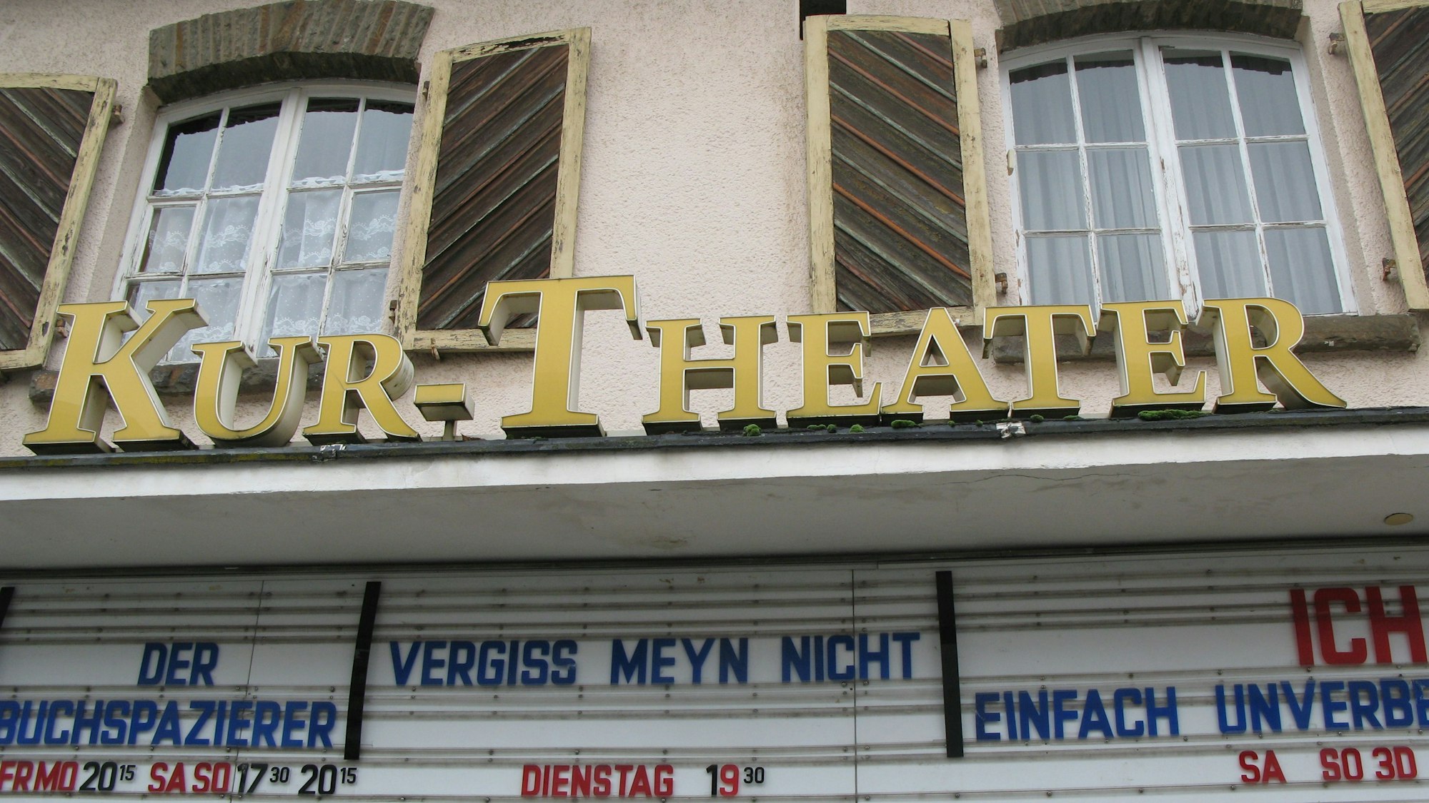 Hausfassade mit zwei Fenstern, Kinofilm-Reklame und Kur-Theater-Schriftzug.