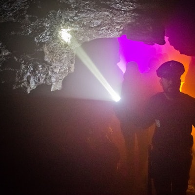Ein Mann mit einer Taschenlampe führt eine Gruppe Menschen durch eine dunkle Höhle.