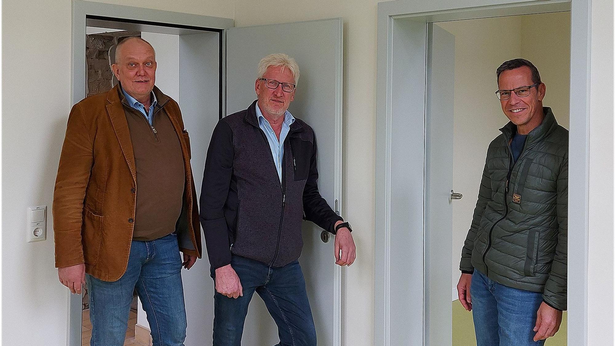 Drei Männer stehen vor zwei geöffneten Türen in einer neuen Wohnung.