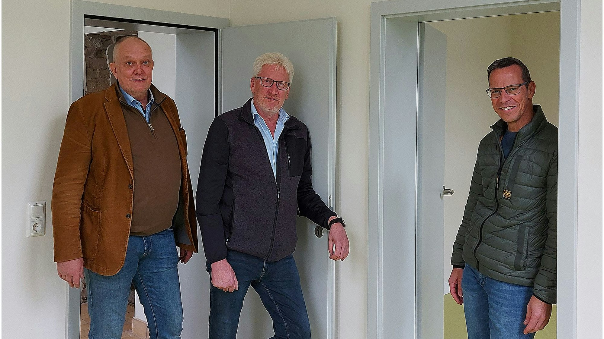 Drei Männer stehen vor zwei geöffneten Türen in einer neuen Wohnung.