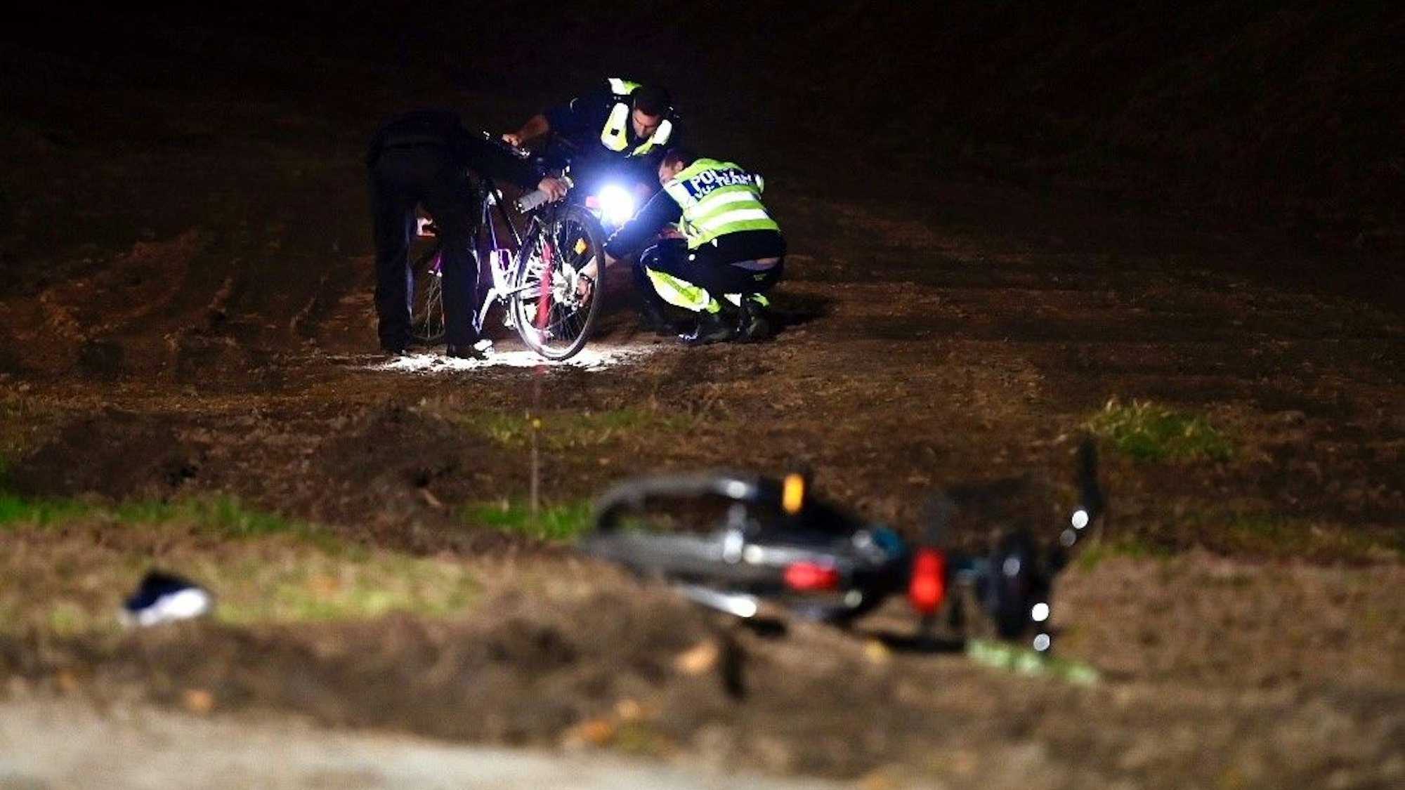 Mehrere Polizisten stehen auf einem Feld. Mit Taschenlampen beleuchten sie ein Fahrrad, ein weiteres liegt im Vorderdrund.