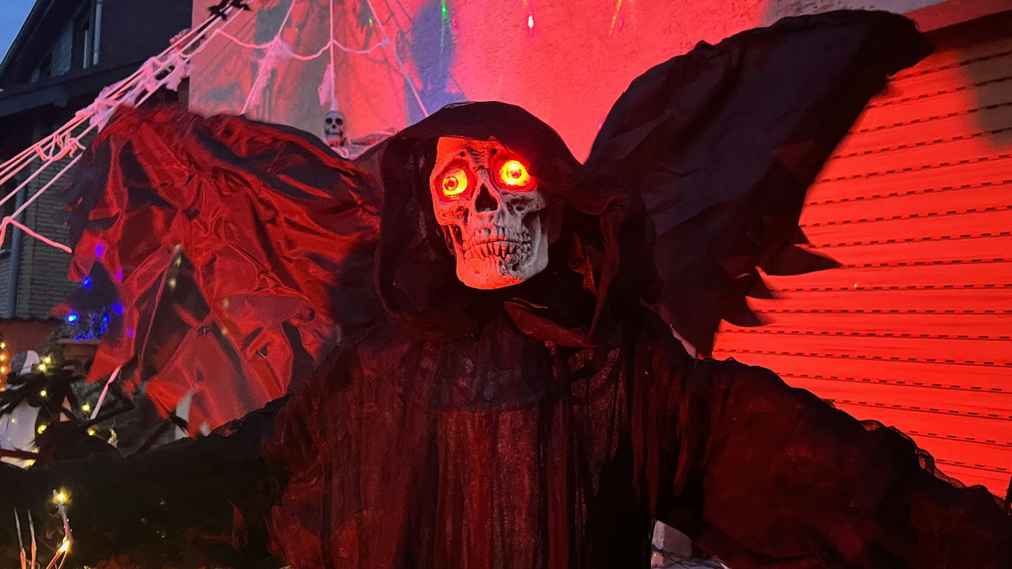Das menschengroße Gespenst steht direkt neben dem Hauseingang. Es ist in einen schwarzen Umhang gehüllt, aus dem Schädel leuchten zwei rote Augen.