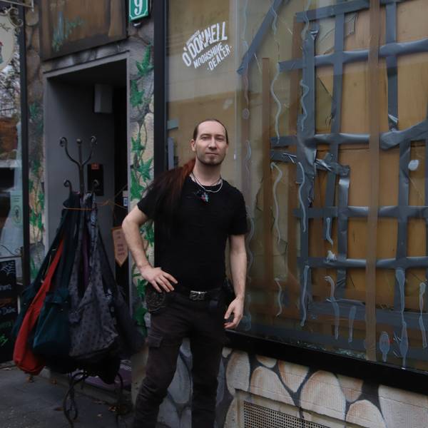 Ein Mitarbeiter steht vor einem Geschäft mit zerschlagener Schaufensterscheibe.