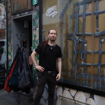 Ein Mitarbeiter steht vor einem Geschäft mit zerschlagener Schaufensterscheibe.