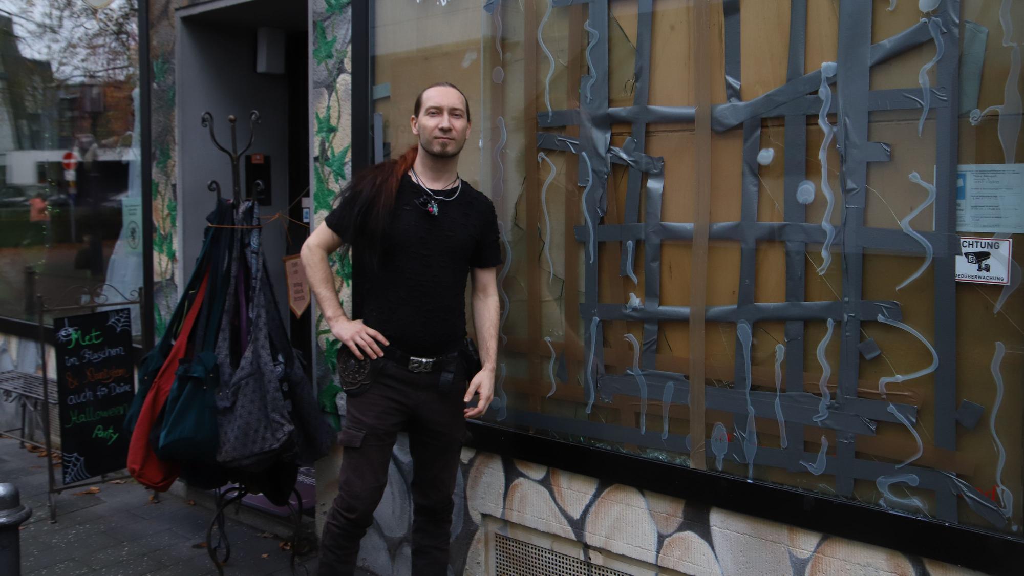 Ein Mitarbeiter steht vor einem Geschäft mit zerschlagener Schaufensterscheibe.