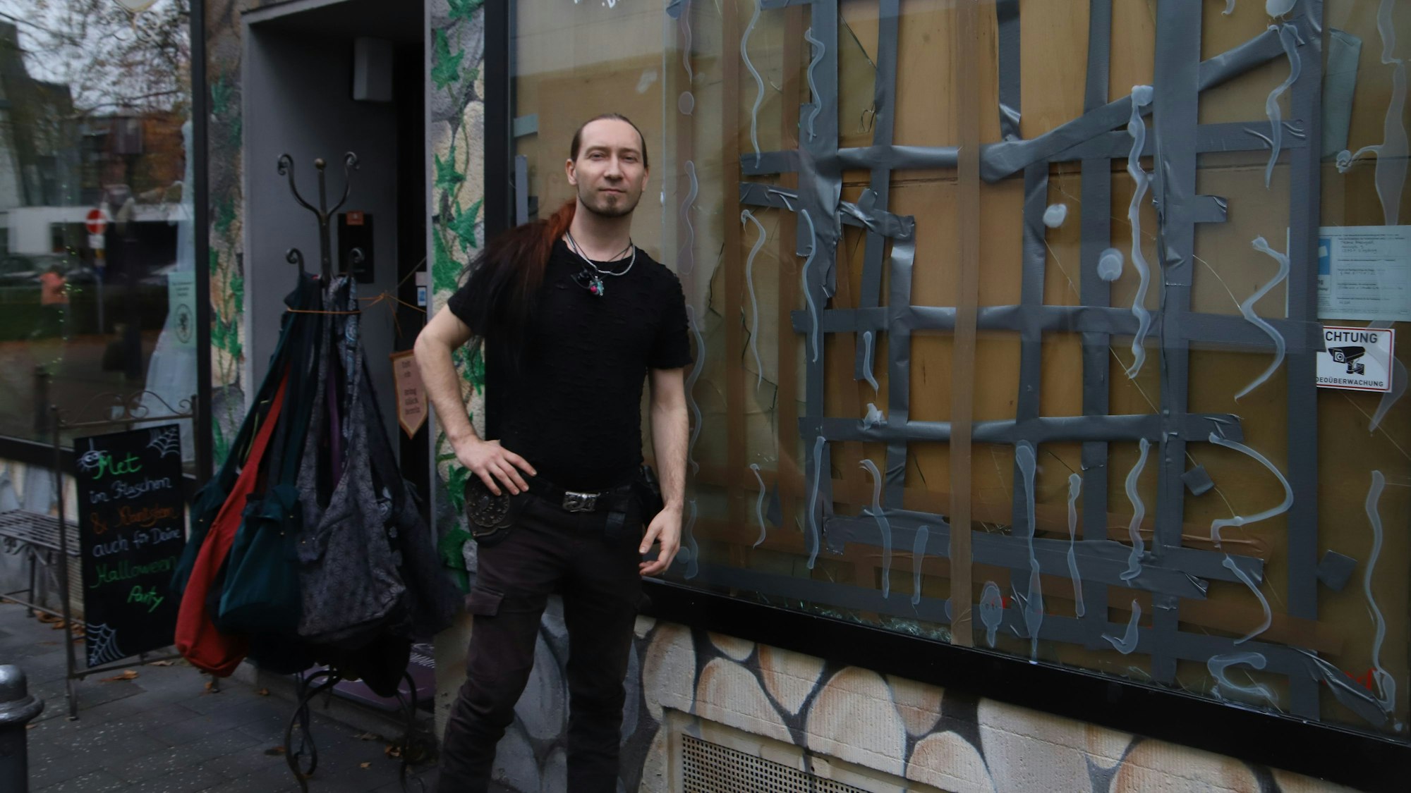 Ein Mitarbeiter steht vor einem Geschäft mit zerschlagener Schaufensterscheibe.