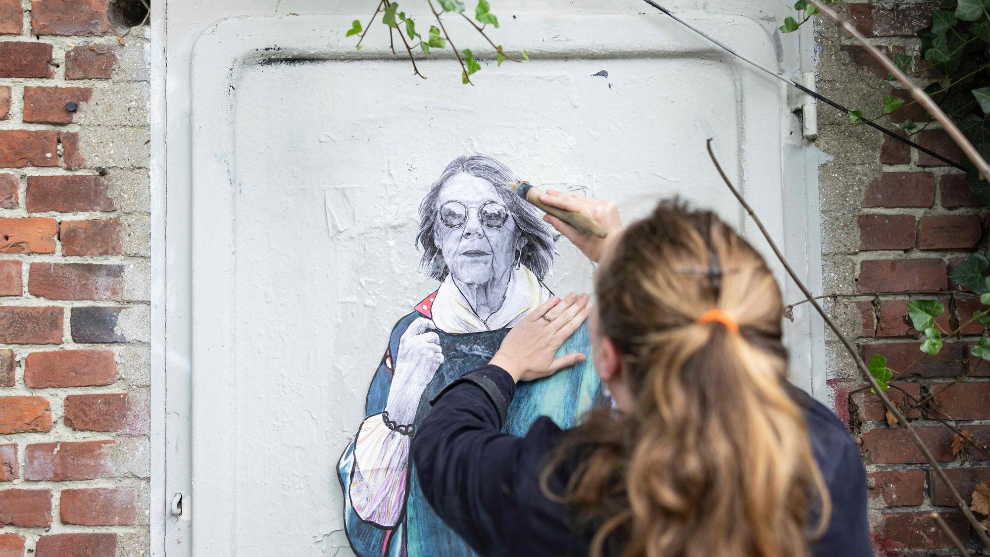 Eine Straßenkünsterlin bringt ein Kunstwerk mit Gisèle Pelicot an.
