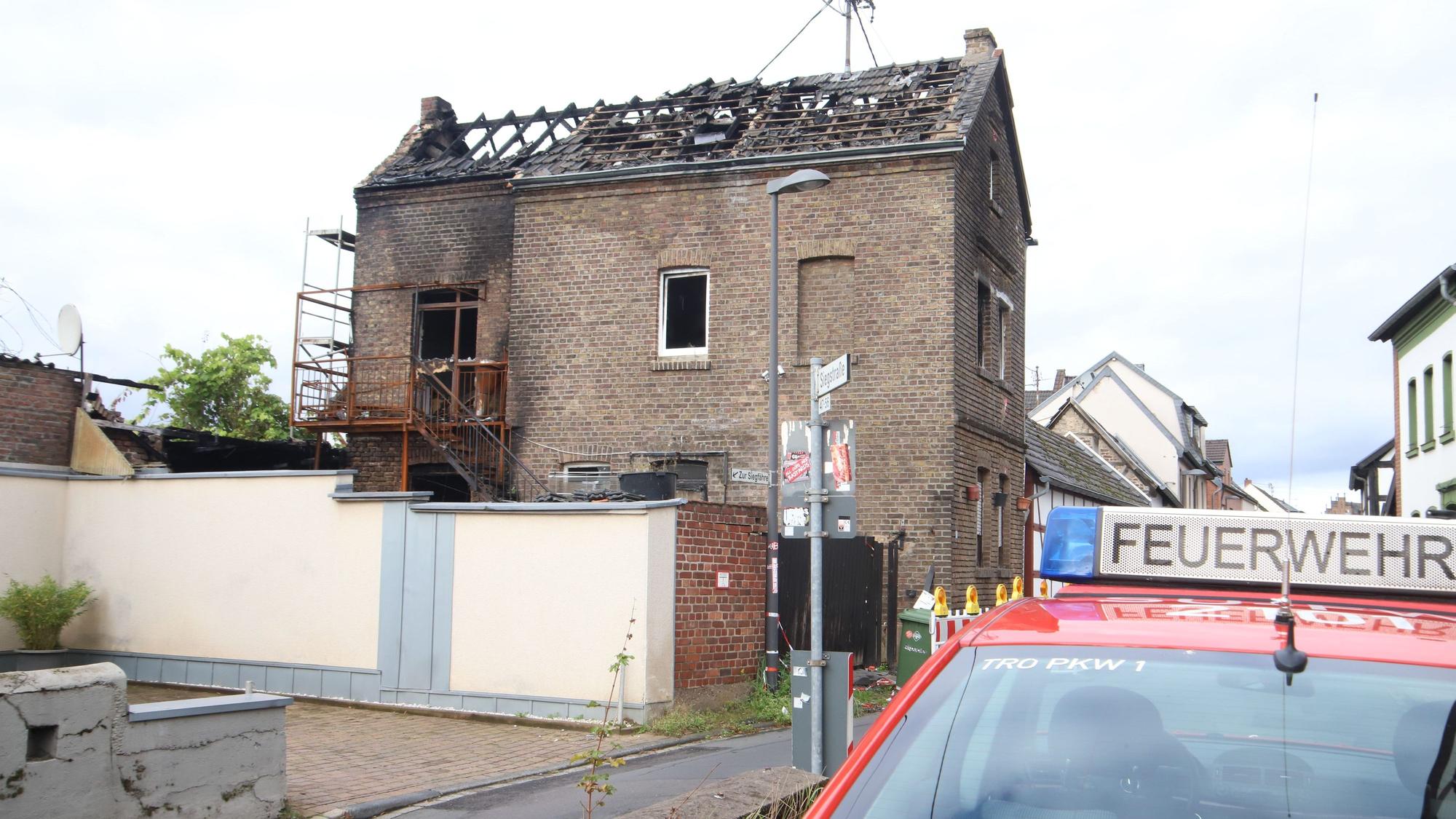 Vor einem ausgebrannten Haus steht ein Feuerwehrwagen.