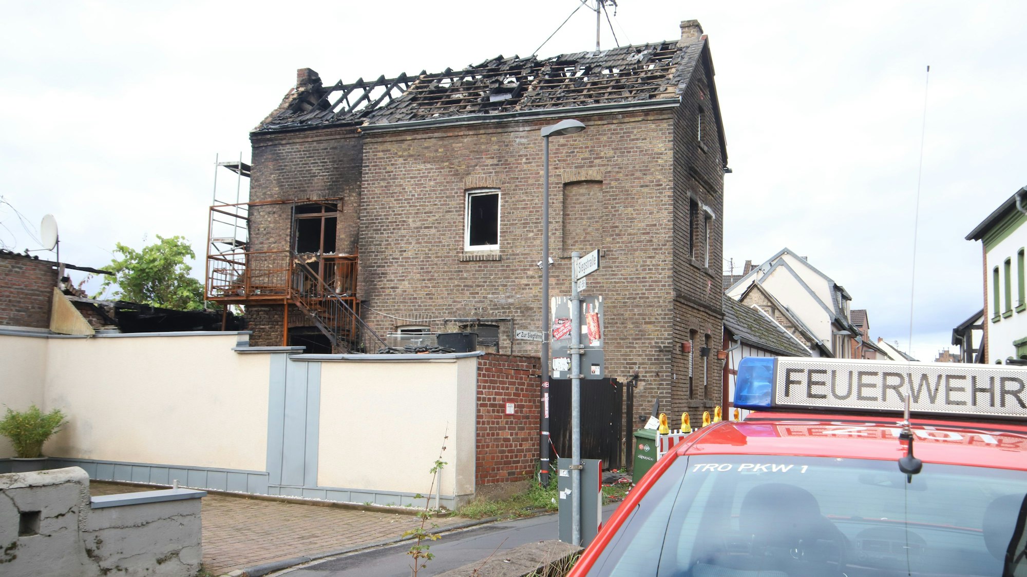 Vor einem ausgebrannten Haus steht ein Feuerwehrwagen.
