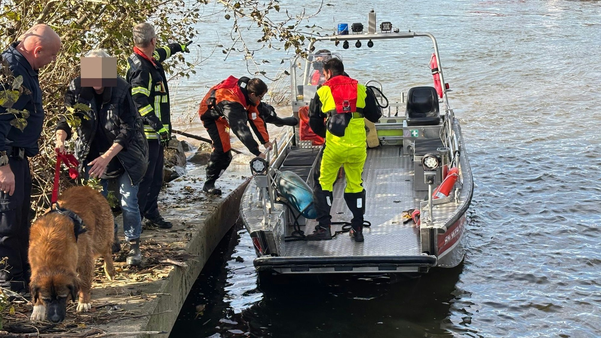 Die Feuerwehr Bonn steigt von einem Boot, daneben ein Hund und seine Besitzerin.