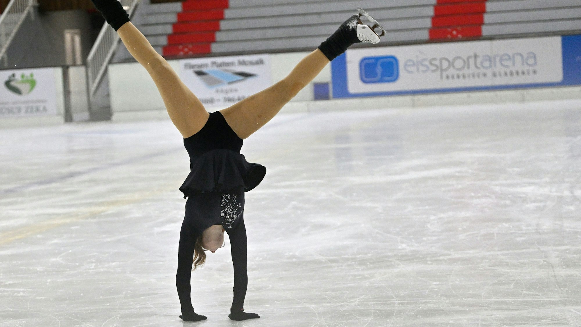 Das Foto zeigt ein Mädchen, das einen Handstand auf dem Eis macht.