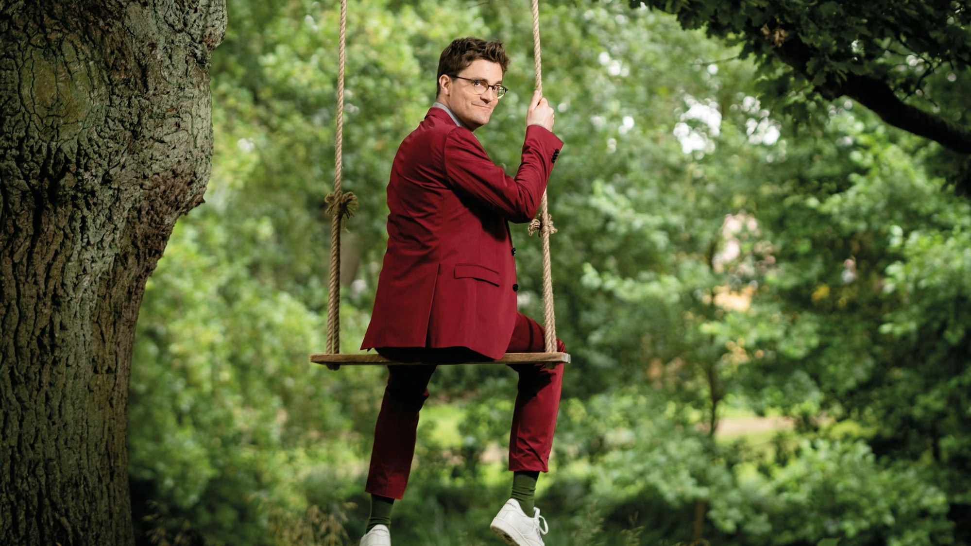 Das Bild zeigt Bodo Wartke auf einer Schaukel, sitzend, Blick über die Schulter.