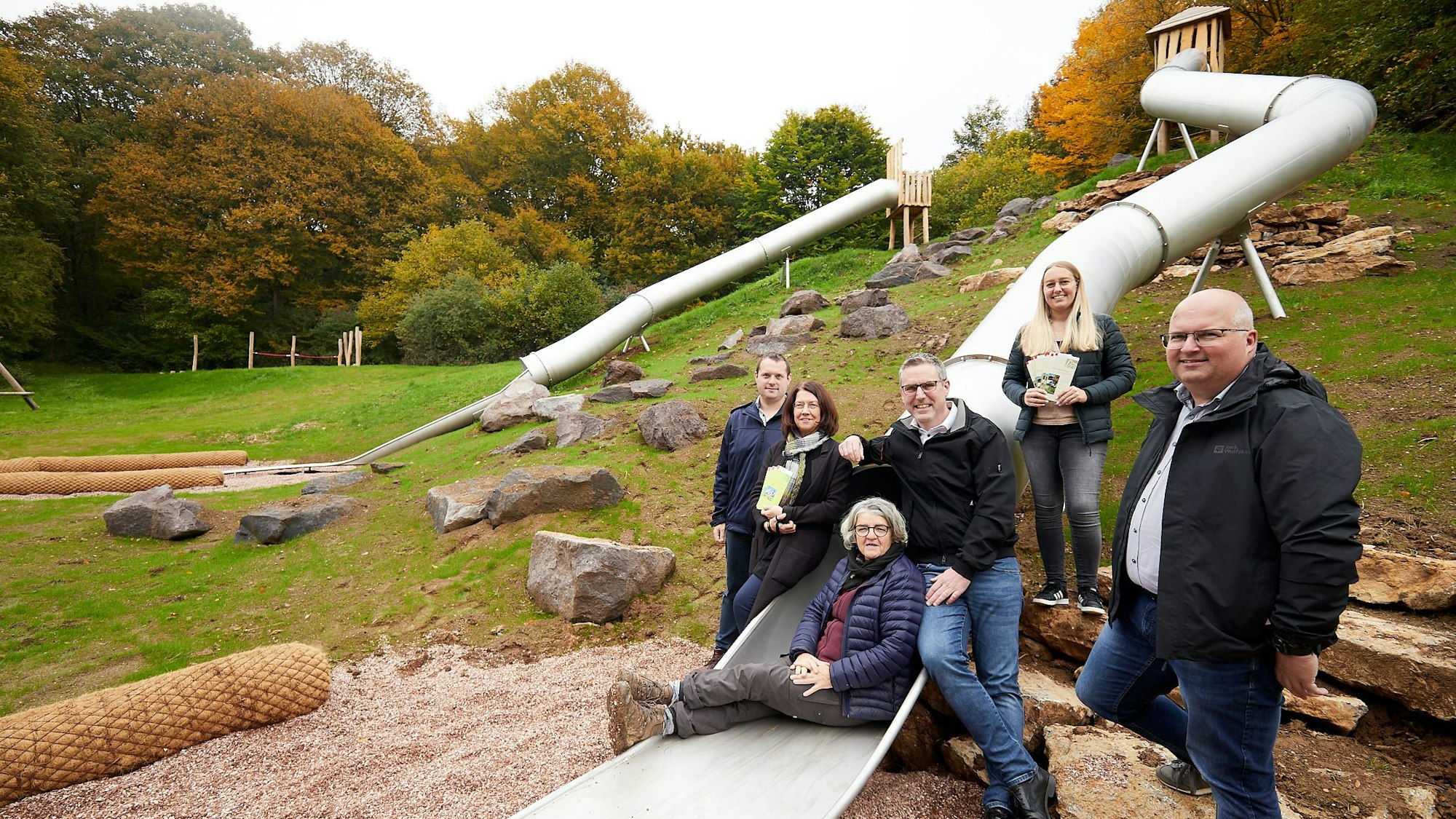 Drei Frauen und drei Männer stehen an und sitzen auf einer langen Rutsche. Sie ist Teil des Abenteuerspielplatzes in Nettersheim.