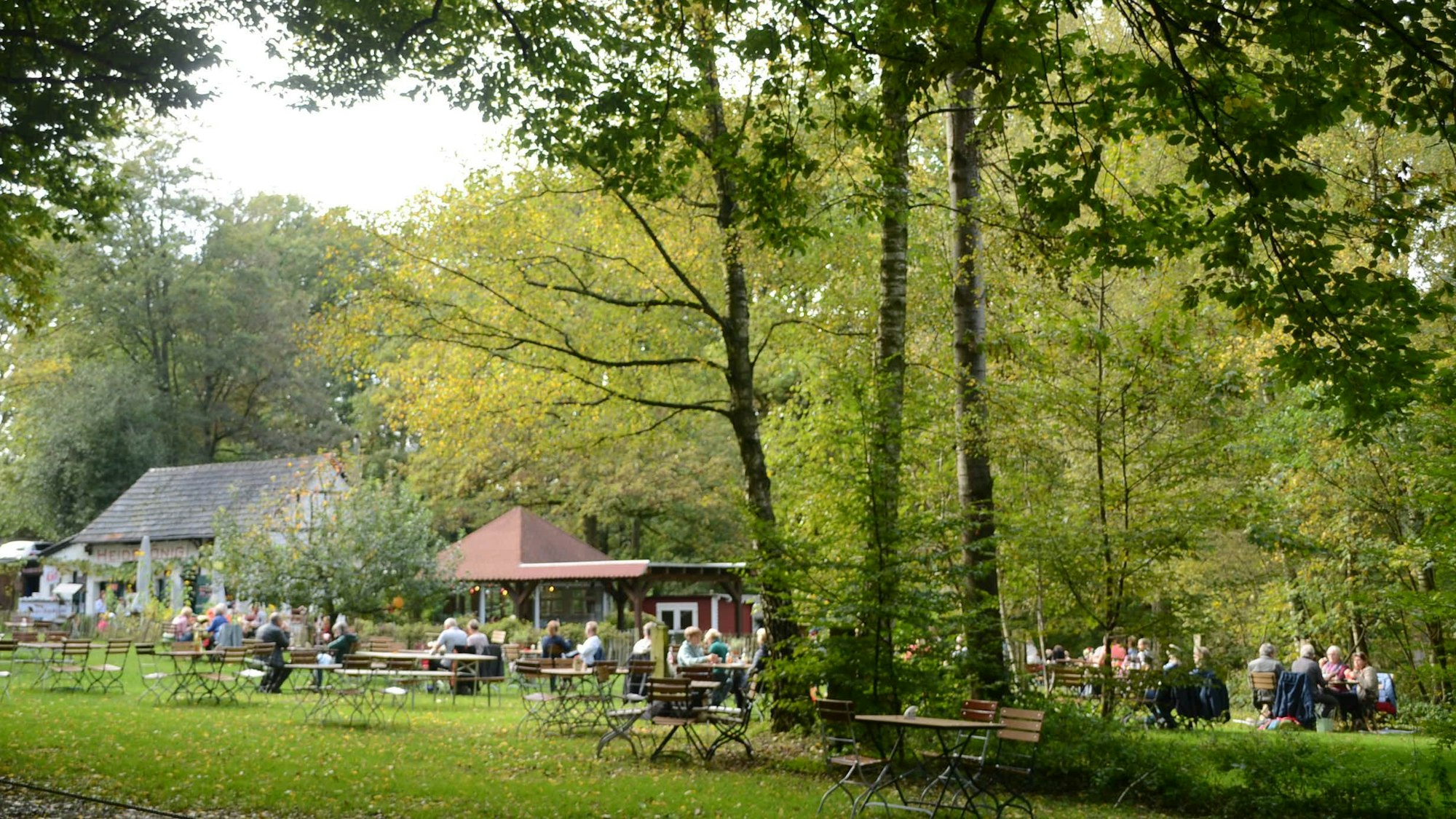 Ein Lokal mit Ausschank auf einer großen Wiese unter hohen Bäumen.