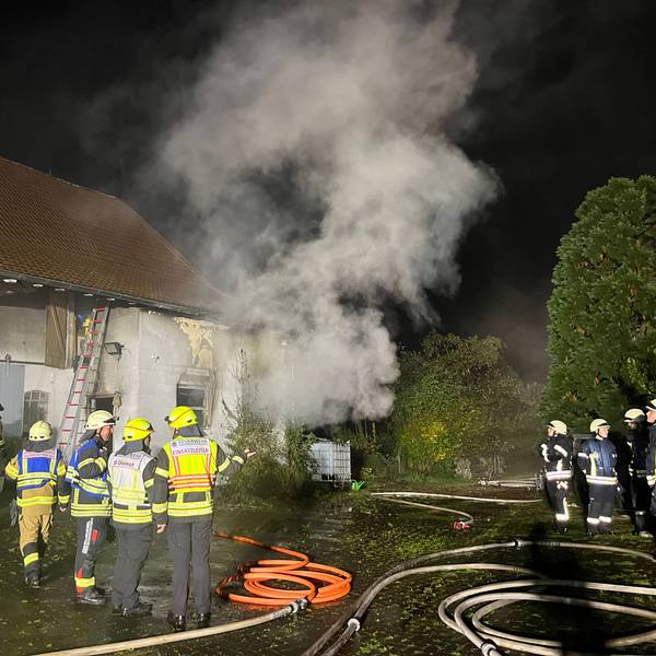 Feuerwehrleute stehen vor einem Gebäude, aus dem es raucht.