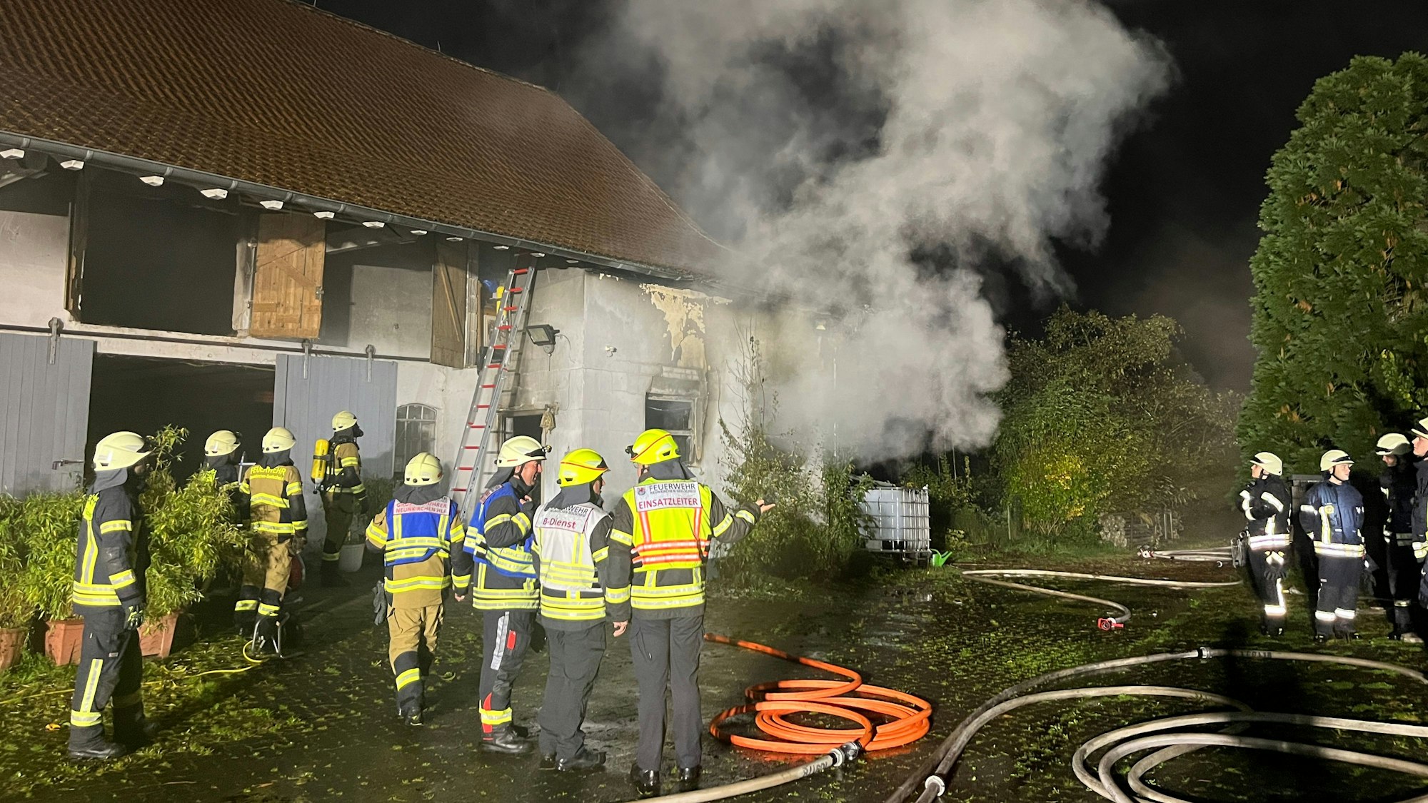 Feuerwehrleute stehen vor einem Gebäude, aus dem es raucht.
