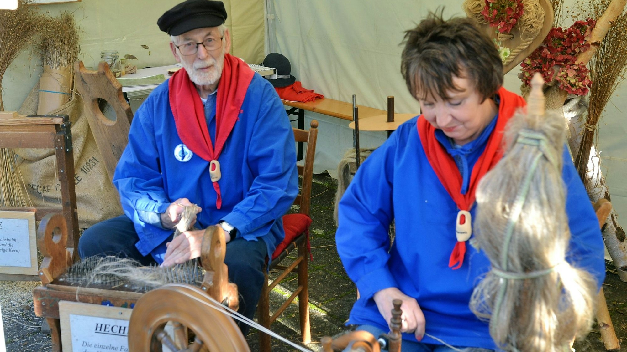 Verena Rentmeister und Hans Röpke tragen blaue Kittel und zeigen die Verarbeitung von Flachs zu Leinen.