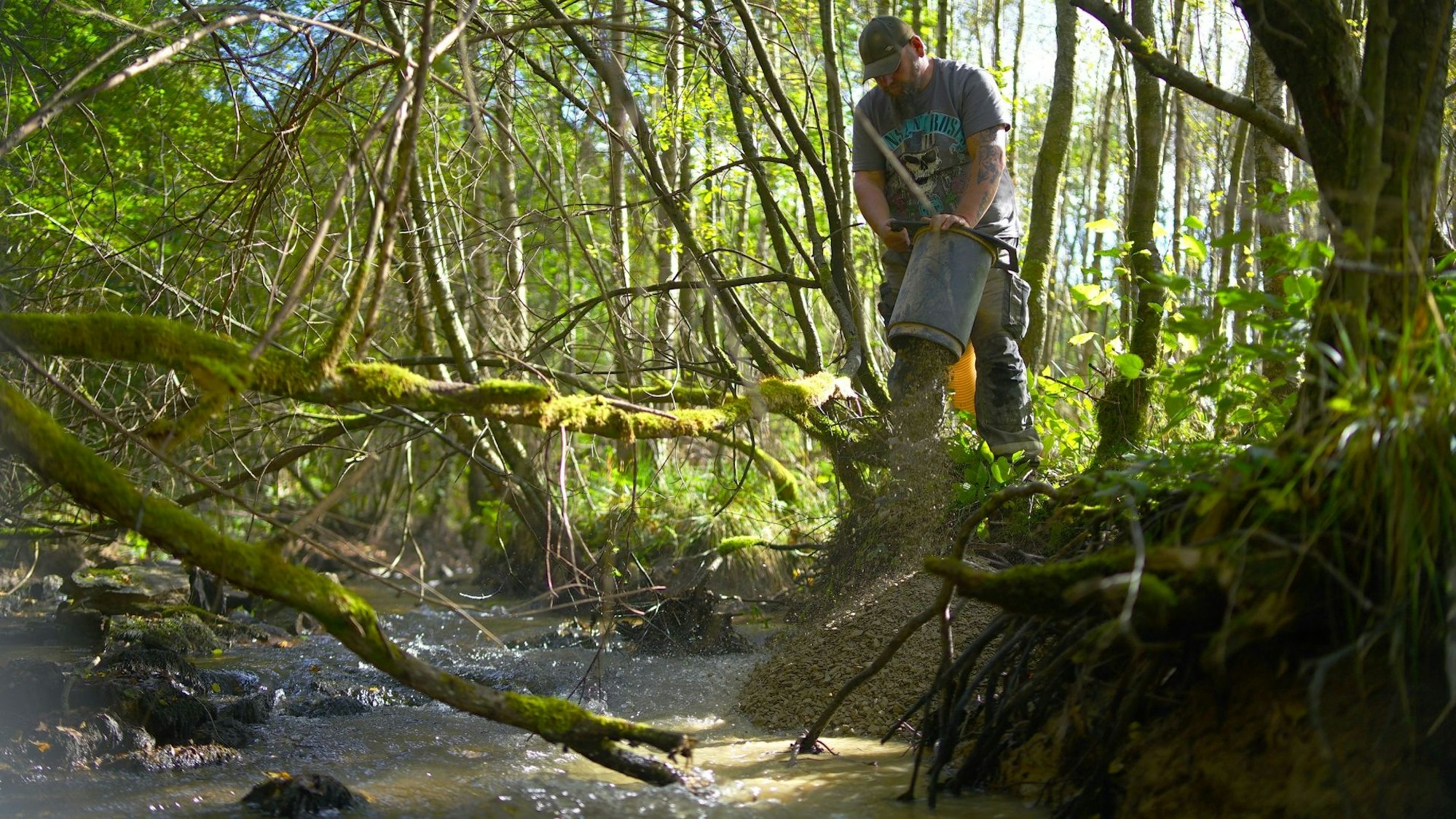 Mithilfe eines Saugbaggers leitet ein Arbeiter Kies in einen Bach.