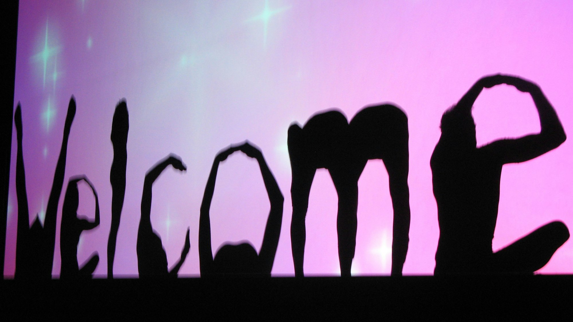 Zu Buchstaben geformte Körper bilden im Schattenriss das Wort Welcome.
