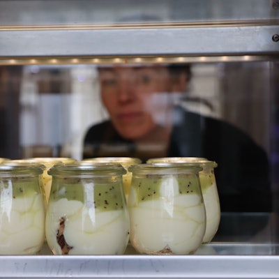 Gläschen stehe hinter einer Scheibe, eine Frau schaut durch die Scheibe.