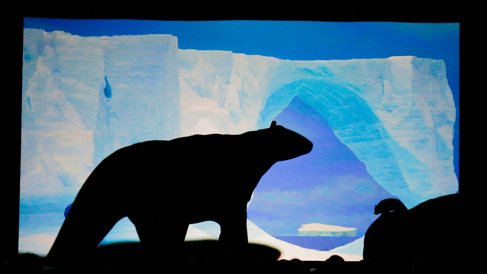 Auf einer Leinwand ist vor einer gemalten Polarlandschaft die Silhouette eines Eisbären zu sehen.