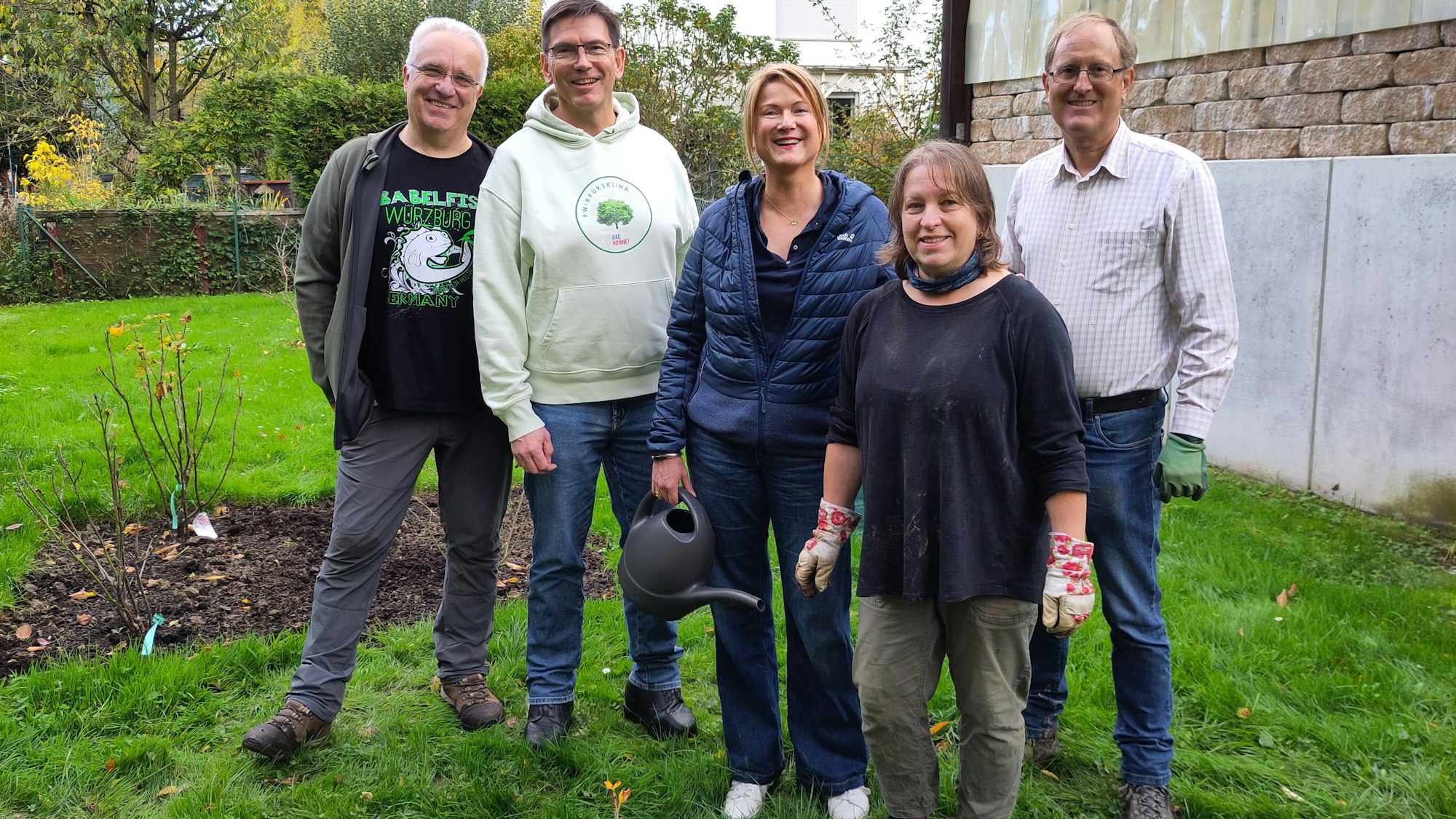 Eine Gruppe von Menschen auf einer Rasenfläche, ein Frau hält eine kleine Gieskanne.