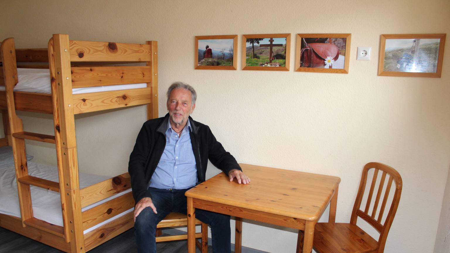 Ein älterer Herr sitzt an einem Tisch in einem Herbergszimmer.