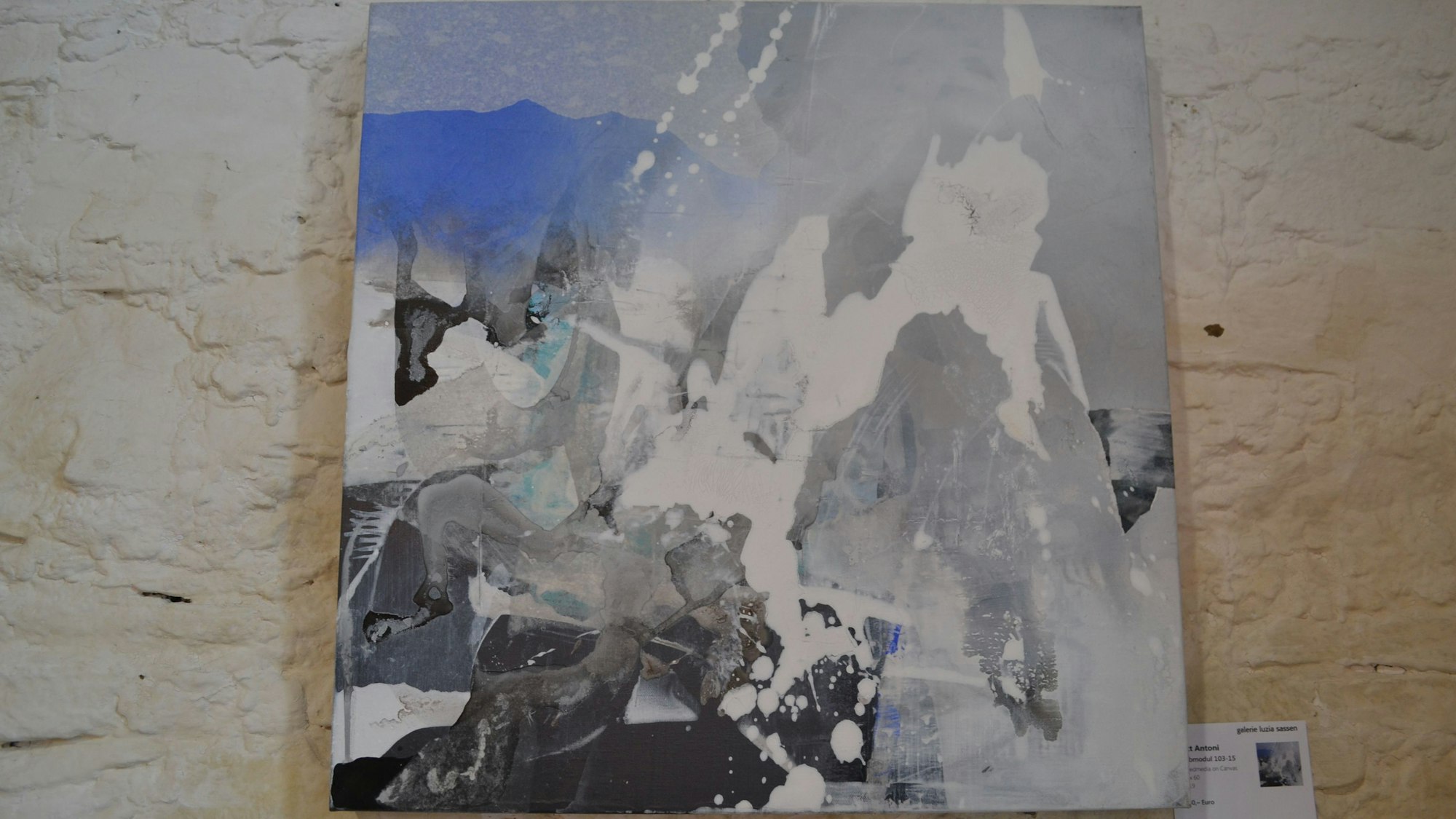 Ein abstraktes Bild an einer Wand mit den Farben Blau, Grau, Schwarz und Weiß.