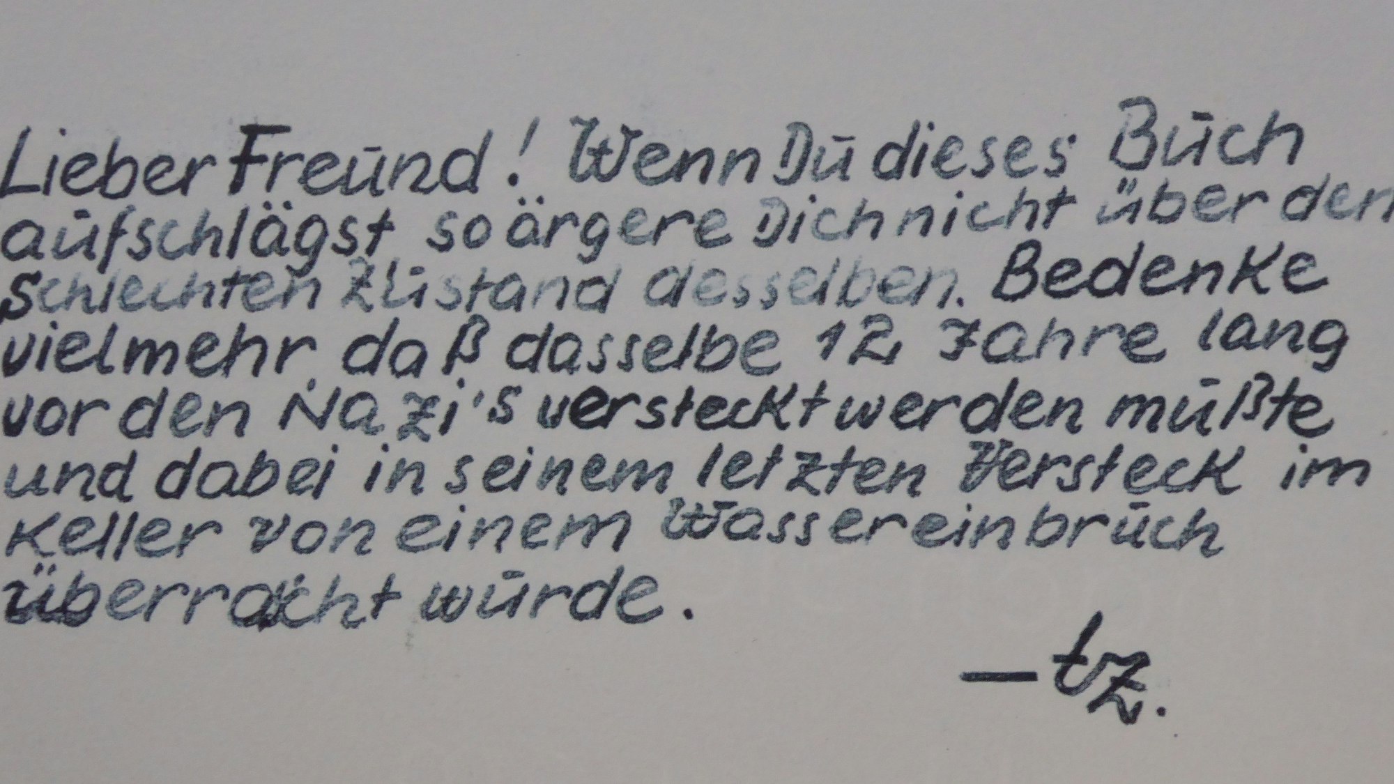 Eine handgeschriebene Mitteilung in acht Zeilen. Der Text lautet: Lieber Freund! Wenn du dieses Buch aufschlägst, so ärgere dich nicht über den schlechten Zustand desselben. Bedenke vielmehr, dass dasselbe zwölf Jahre lang vor den Nazis versteckt werden musste und dabei in seinem letzten Versteck im Keller von einem Wassereinbruch überrascht wurde.