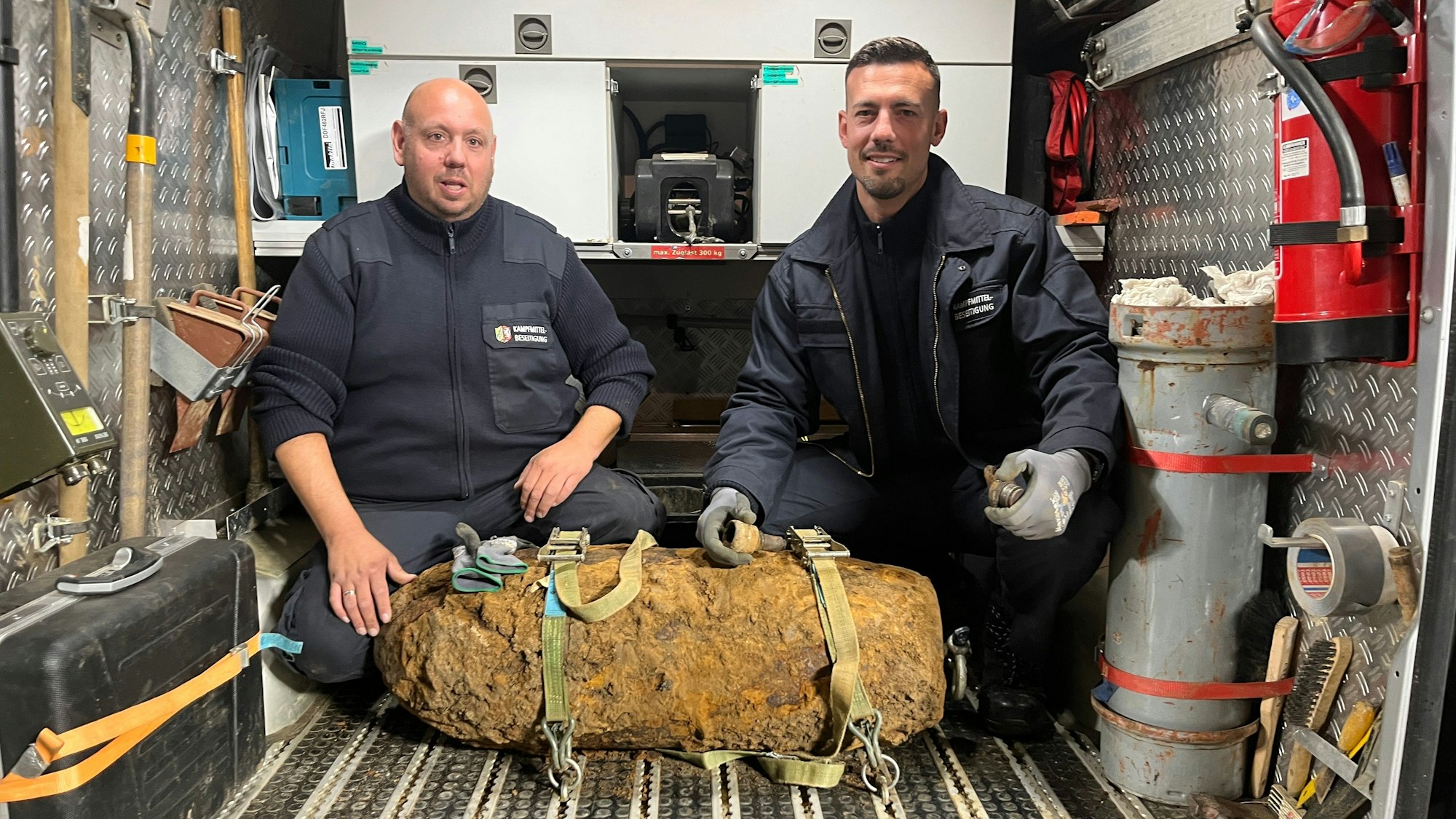 Zwei Männer knien hinter einer alten Bombe in einem Lieferwagen.