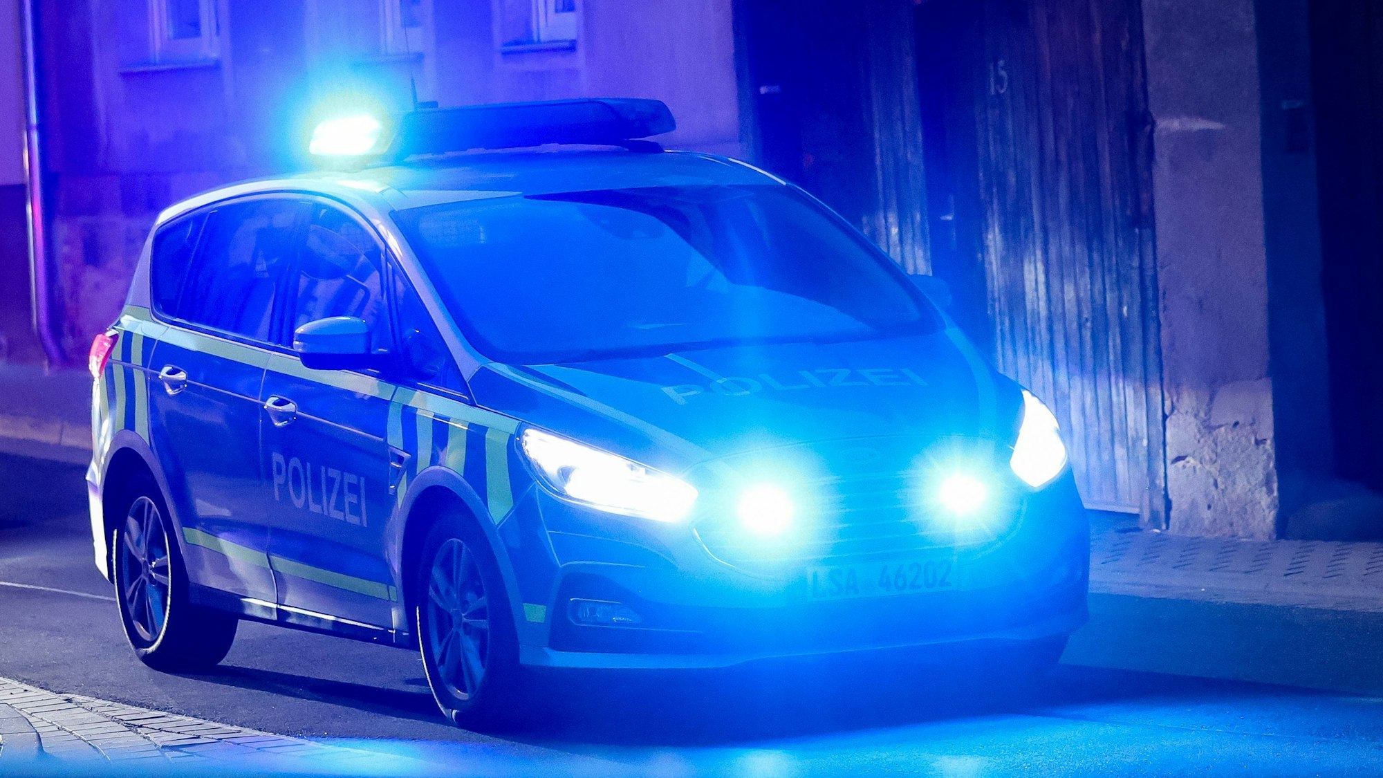 Ein Fahrzeug der Polizei fährt mit Blaulicht am Abend durch eine enge Straße.