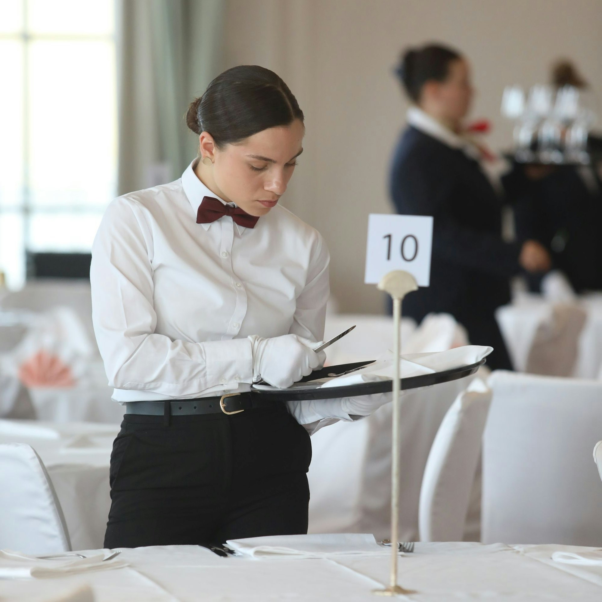 Eine junge Frau deckt einen Tisch ein, auf dem ein Ständer mit der Zahl zehn steht.