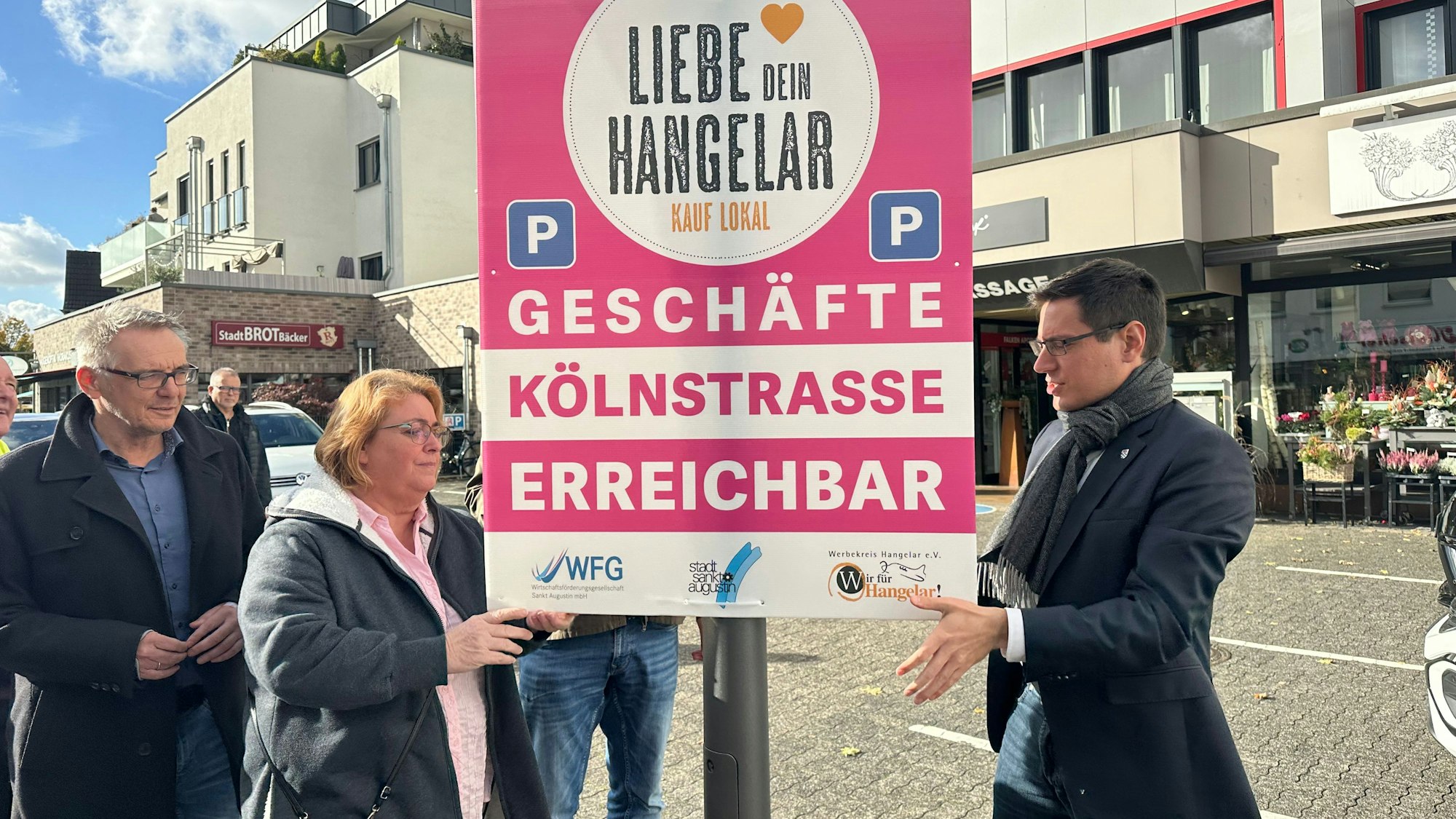 Die Kölnstaße in Hangelar ist durch Tiefbauarbeiten teilweise gesperrt. Mit einer Aktion soll für die Geschäfte dort geworben werden. Rainer Gleß, Natascha Brecht-Kalus und Bürgermeister Max Leitterstorf (v.l.) hängen ein Plakat auf.