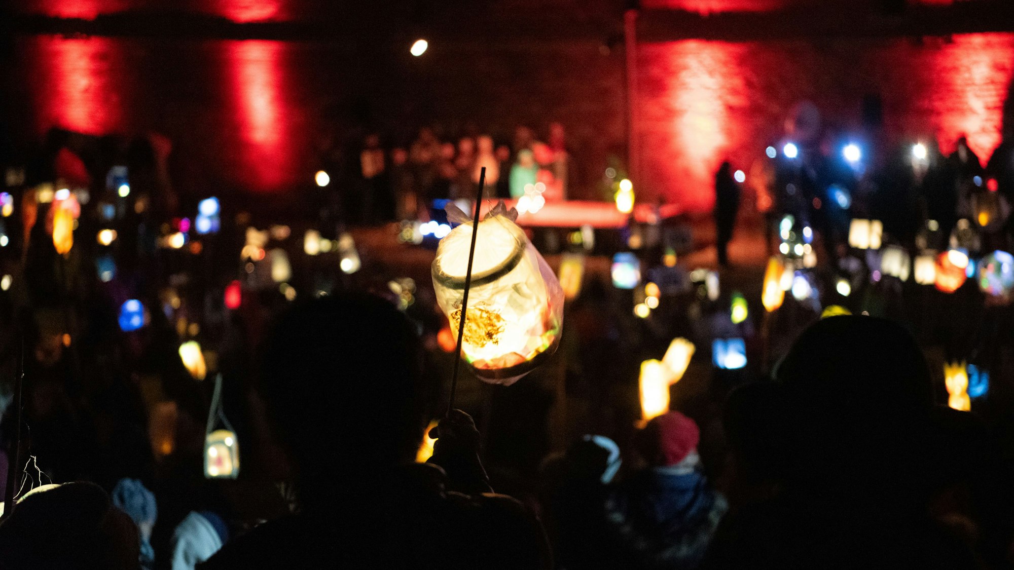 Eine Laterne wird vor der Zülpicher Burg hochgehalten, im Hintergrund leuchten noch mehr Laternen.