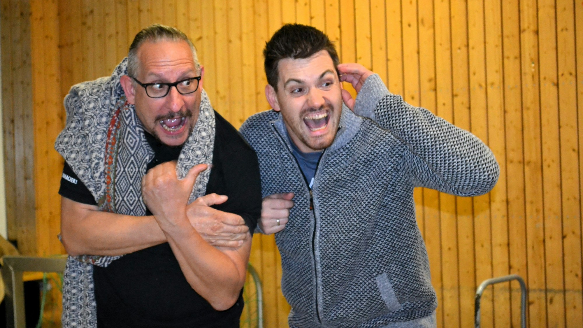 Zwei Männer mit weit aufgerissenem Mund bei einer Theaterprobe.
