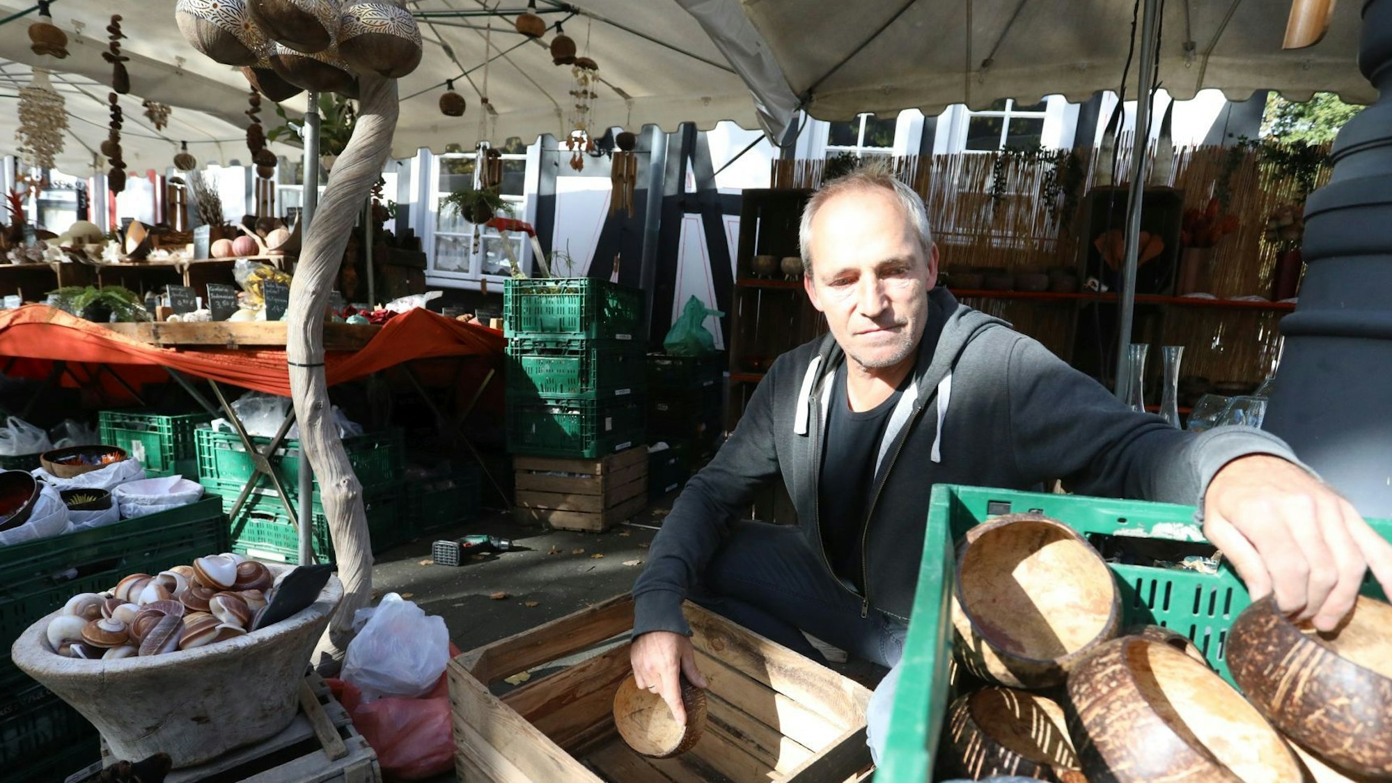 Ein Mann räumt Holzschalen in eine Kiste, im Hintergrund sind verschiedene Deko-Artikel zu sehen.