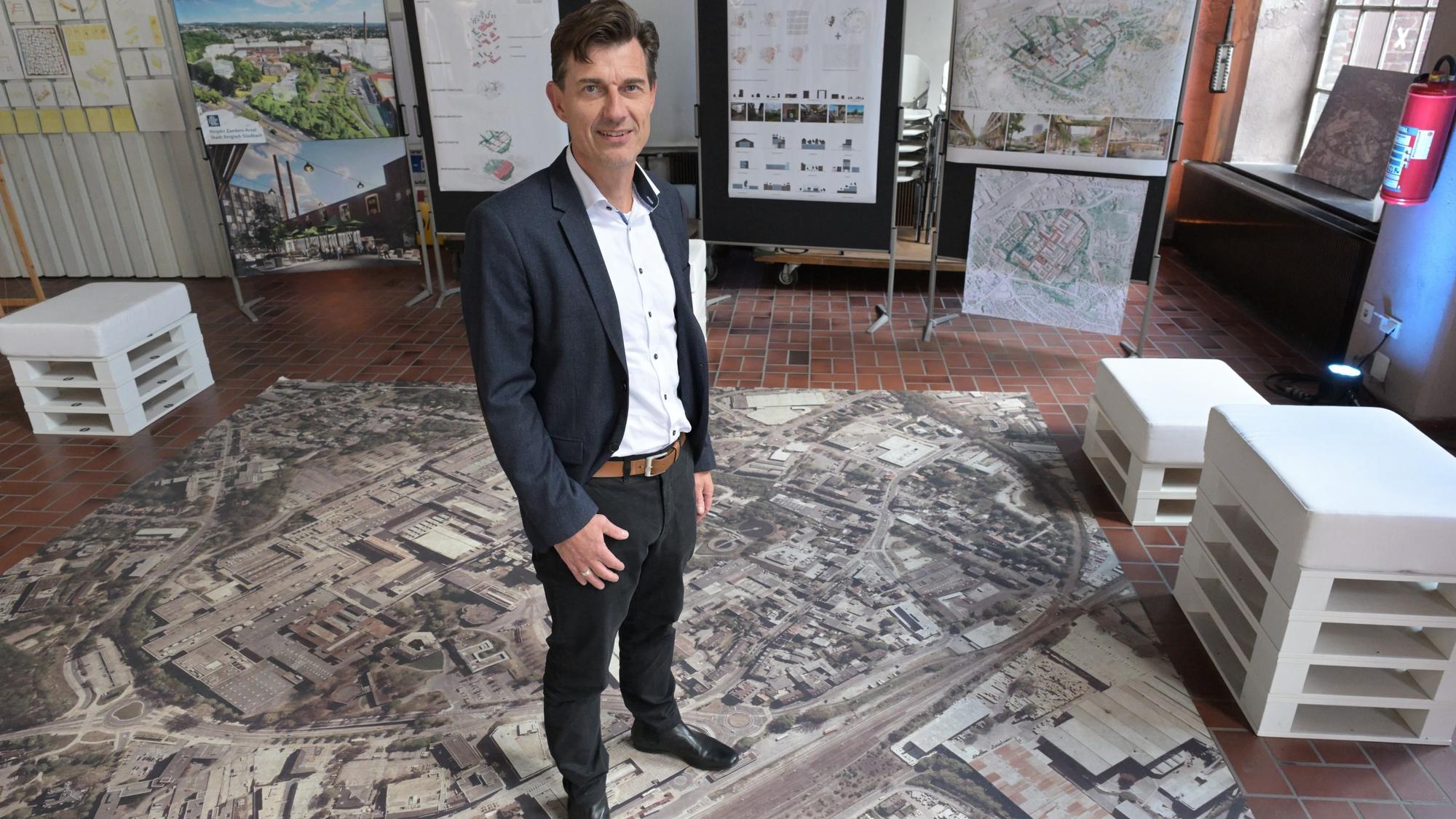 Oliver Brügge bei seiner Vorstellung im Oktober 2024. Er steht auf einem Foto der 36 Hektar großen Industriebrache.