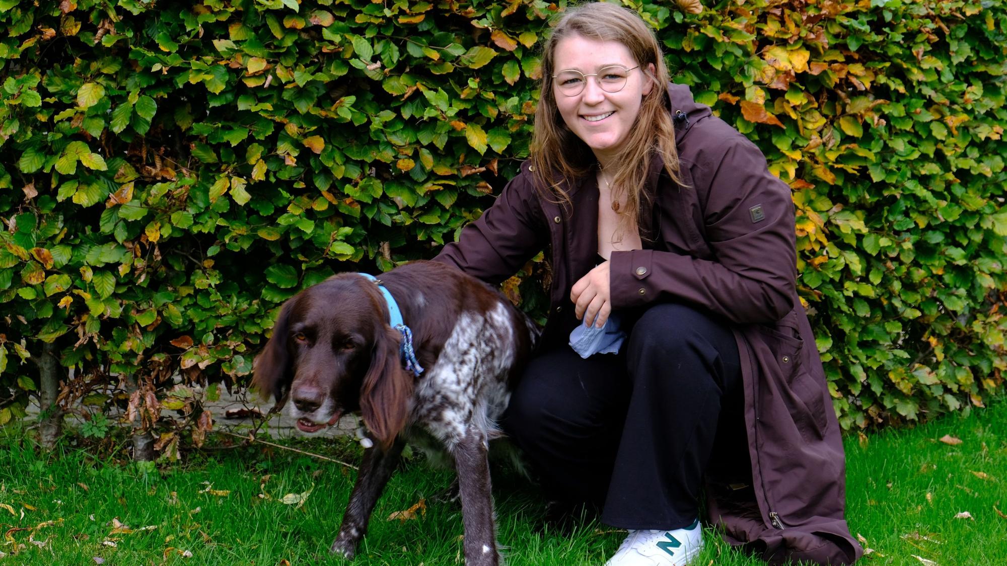 Tessa Riedling kniet mit Deutsch-Langhaar-Hündin Milly vor einer Hecke.