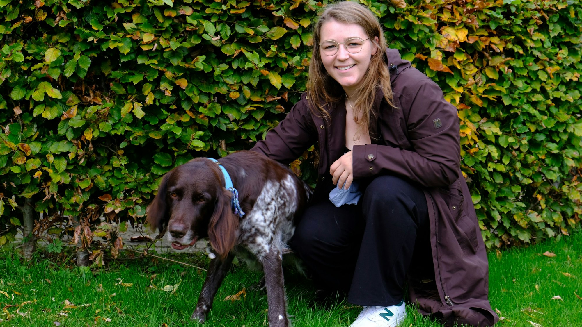 Tessa Riedling kniet mit Deutsch-Langhaar-Hündin Milly vor einer Hecke.